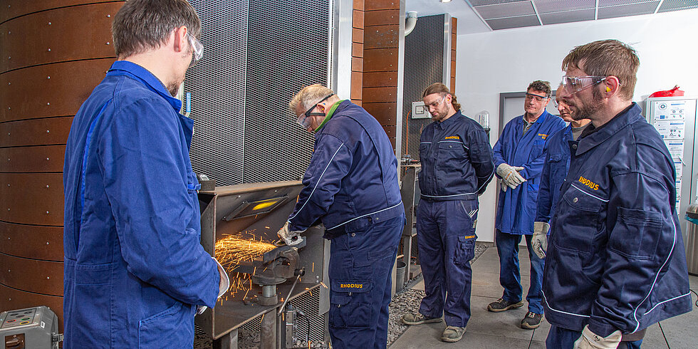 Technik pro aplikaci předvádí v kompetenčním centru RHODIUS brusný kotouč, několik řemeslníků se dívá