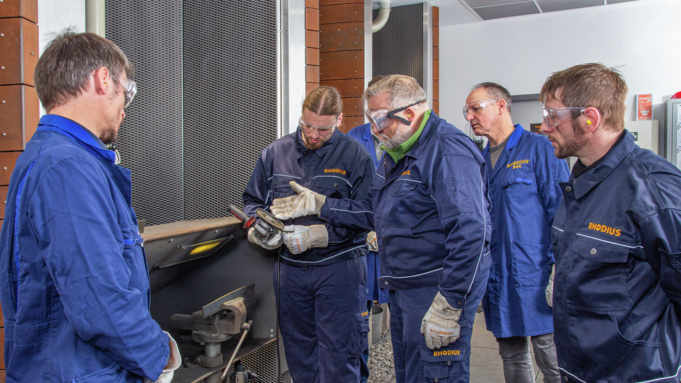 Anwendungstechniker führt im RHODIUS Competence Center eine Schleifscheibe vor, mehrere Handwerker schauen zu